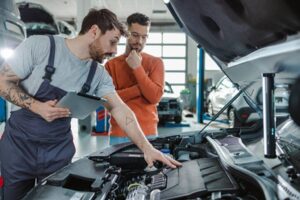 A man is inspecting the car engine in front of the car owner in Surrey,BC